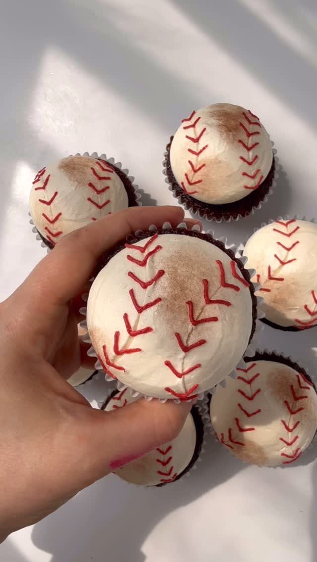 Baseball cupcakes with white frosting and red stitching held by a hand.