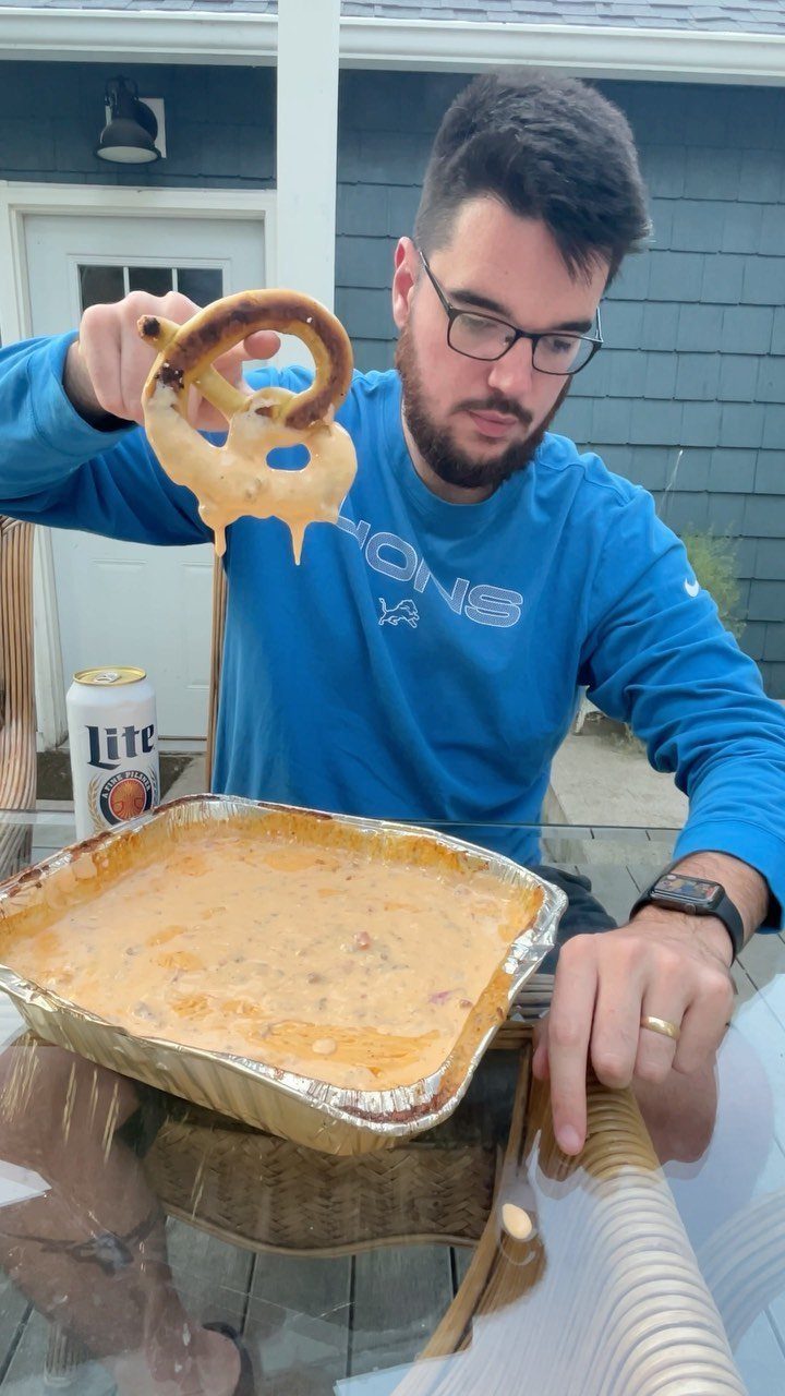 Man dipping a soft pretzel into a pan of creamy beer cheese dip.