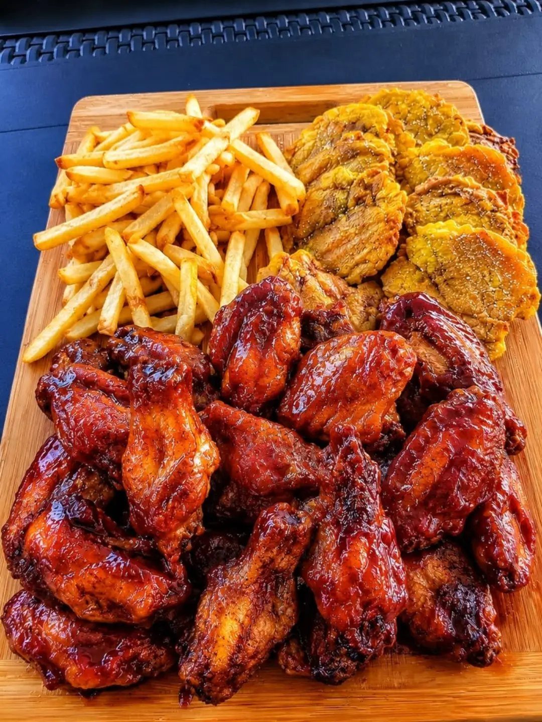 Glazed chicken wings served on a wooden platter with french fries and plantains.
