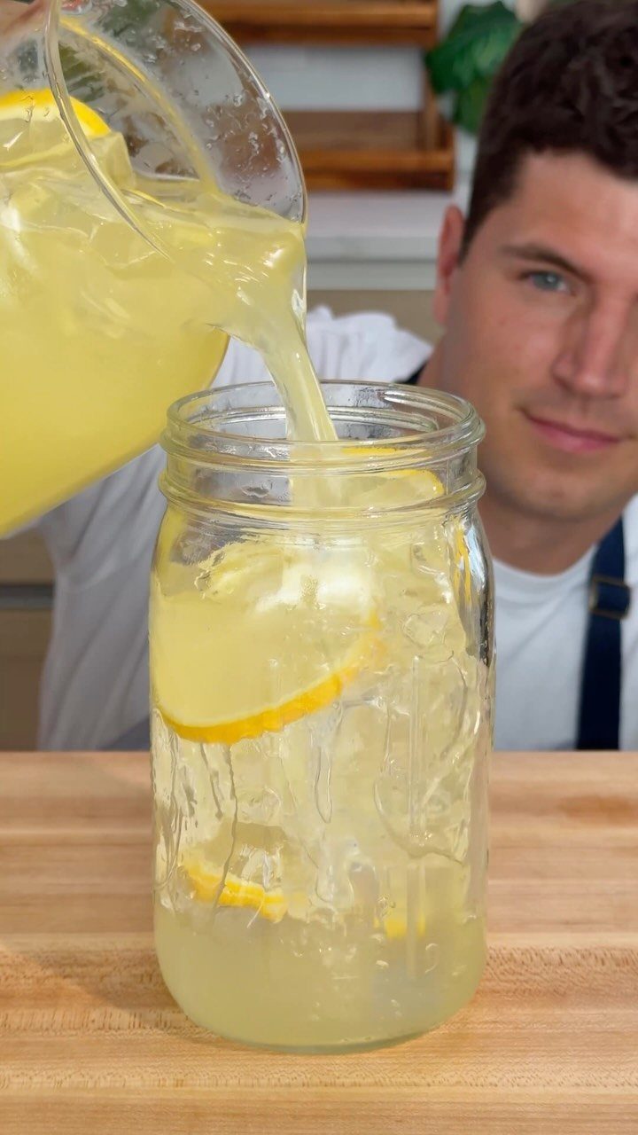 Yellow lemonade being poured into a mason jar with ice and lemon slices.