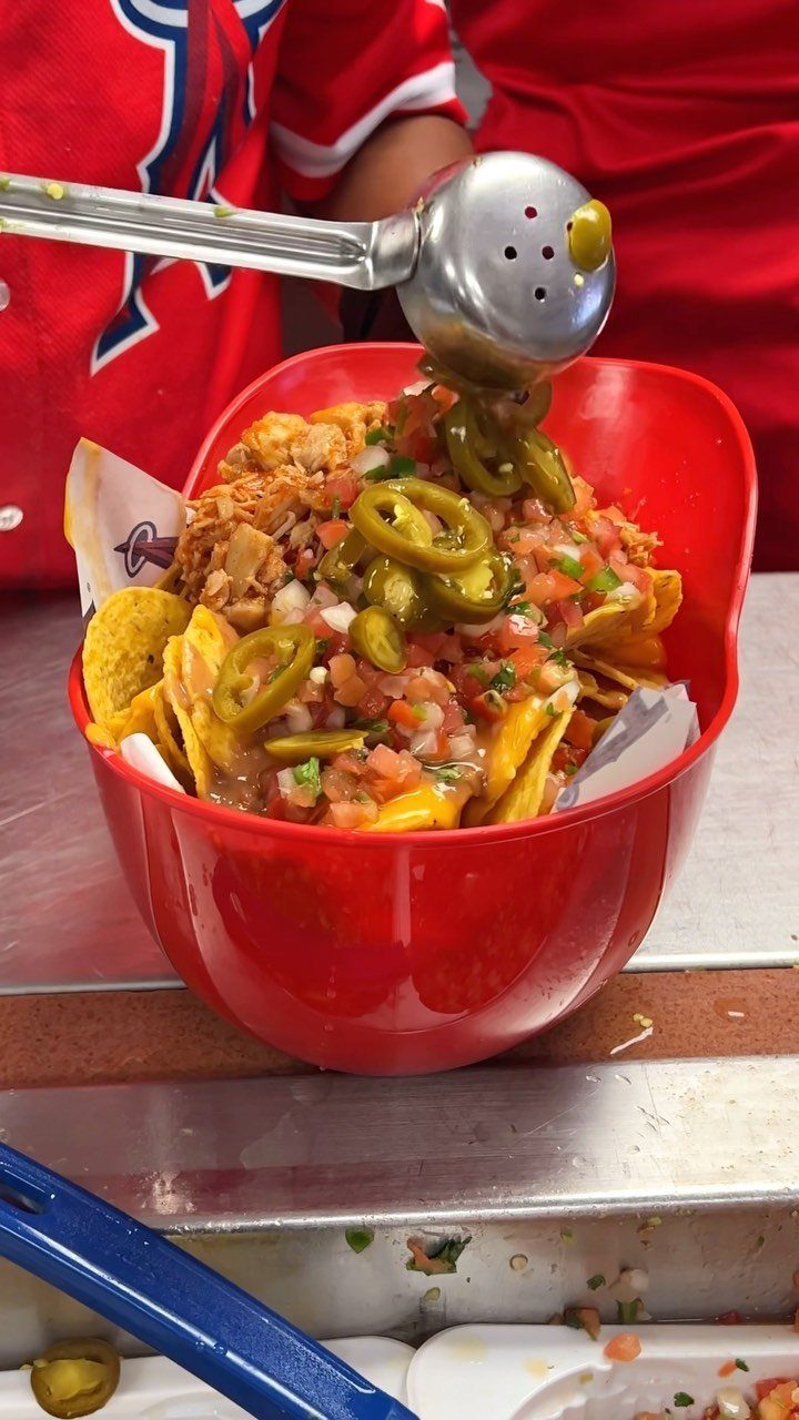 Loaded nachos with cheese, salsa, and jalapeños in a red plastic bowl.