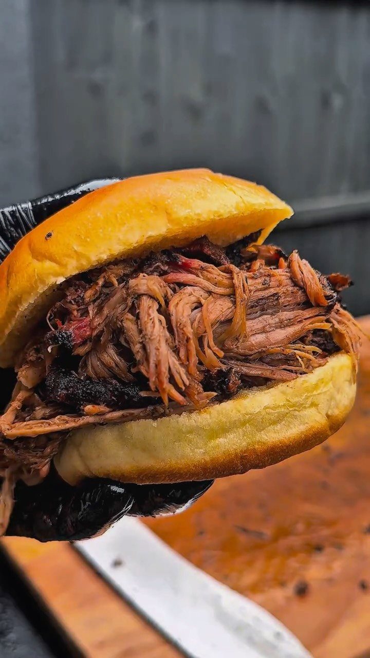 Pulled pork sandwich on a brioche bun held by a gloved hand.