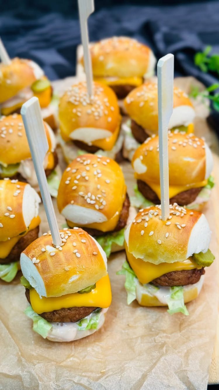 Mini burgers with cheese and lettuce on parchment paper with wooden skewers.