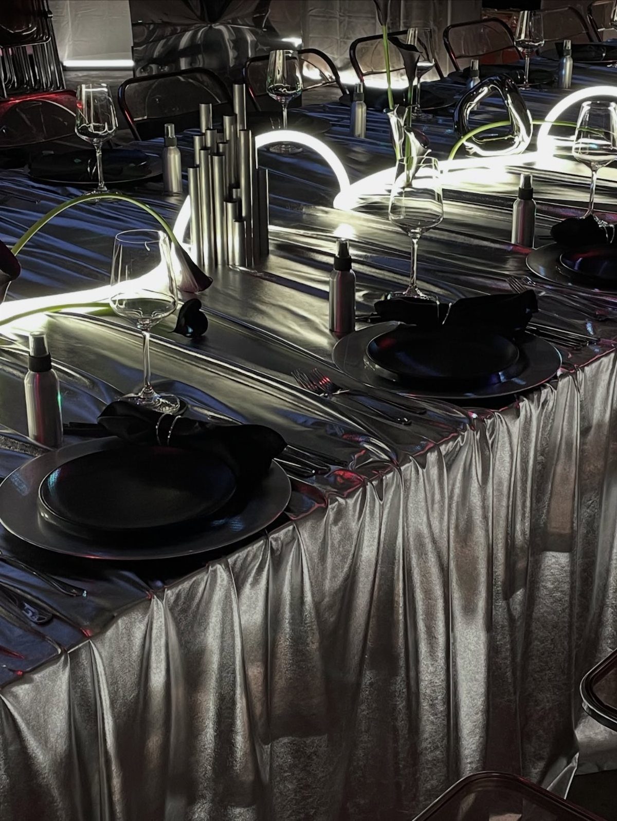 Silver metallic table setting with black plates and glowing white neon light accents.