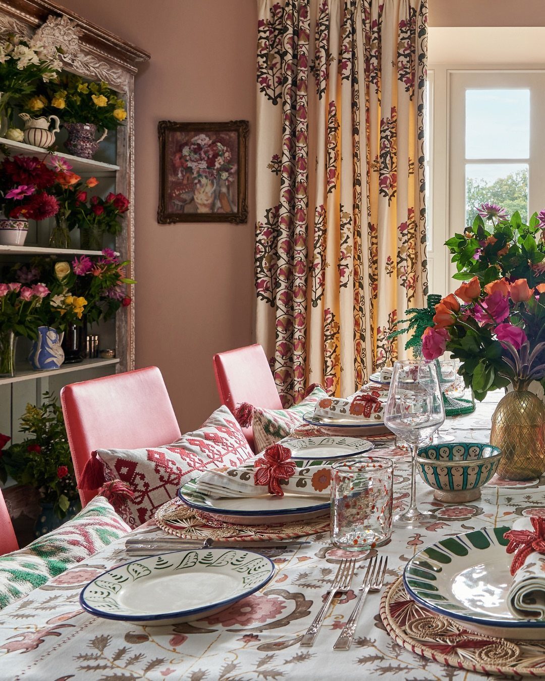 Dining table with floral tablecloth, woven chargers, and colorful flower arrangements.