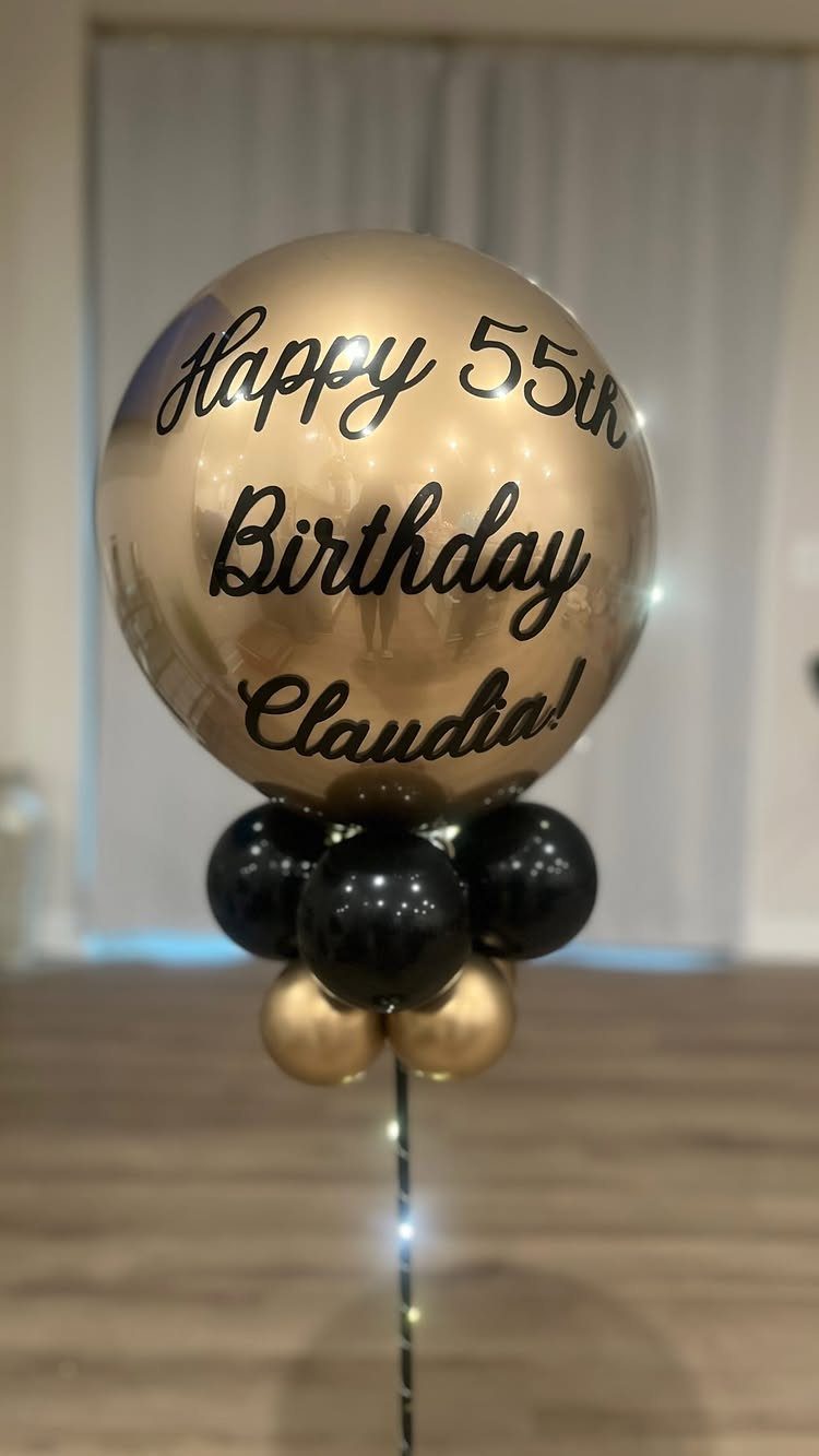 Gold and black balloon centerpiece with personalized birthday message on a stand
