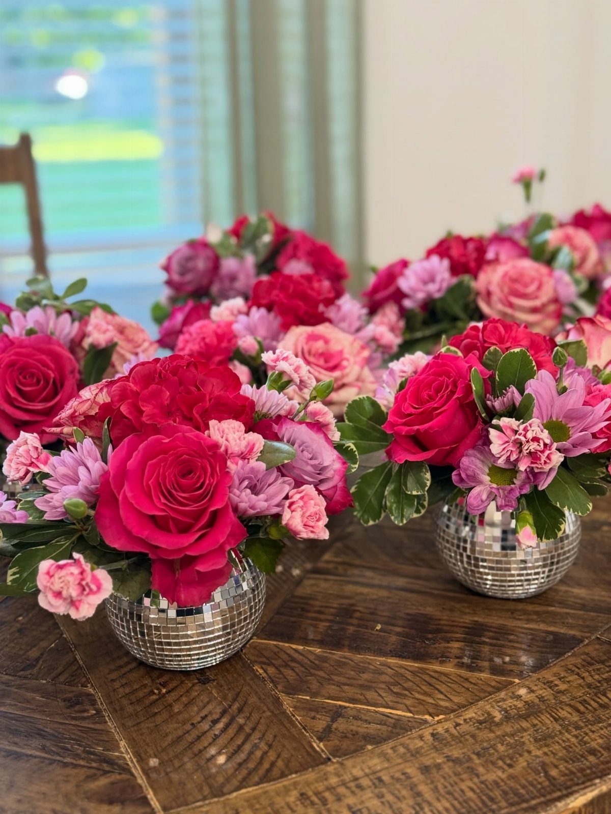Pink and magenta floral arrangements in disco ball vases on a wooden table.