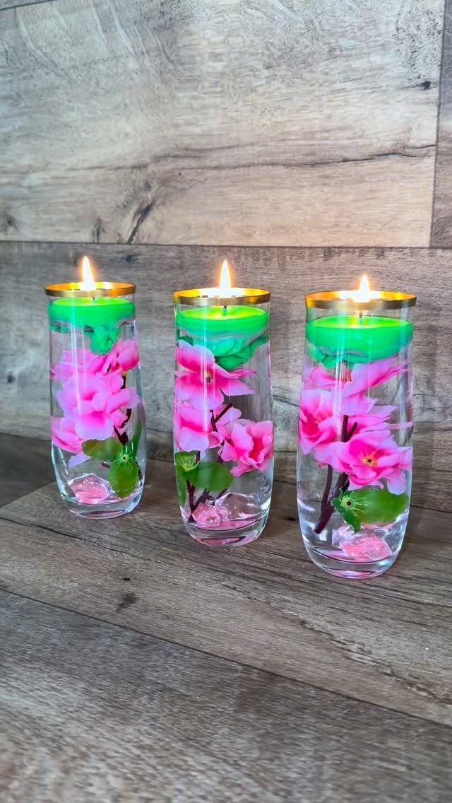 Three floating green candles in glass vases with pink flowers on wooden surface