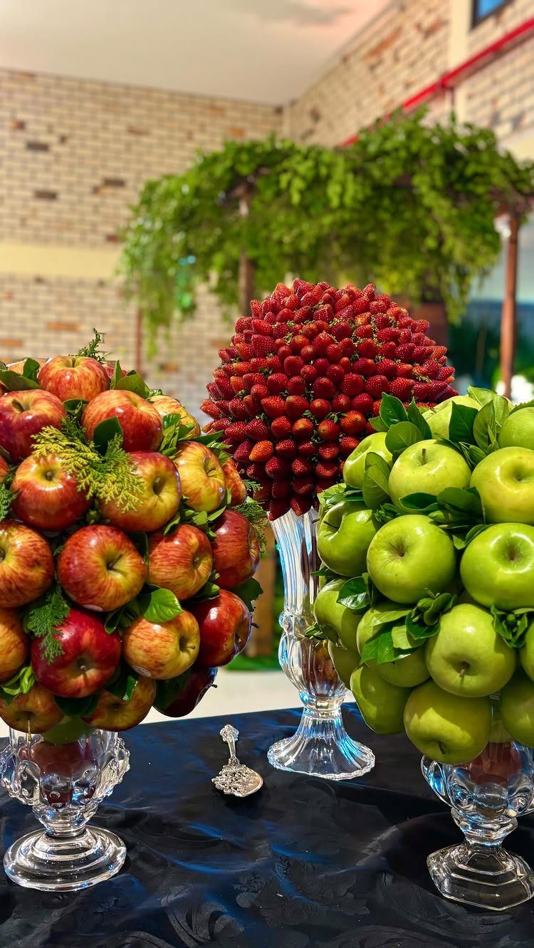 Fruit centerpieces featuring spheres of red apples, strawberries, and green apples in glass vases.