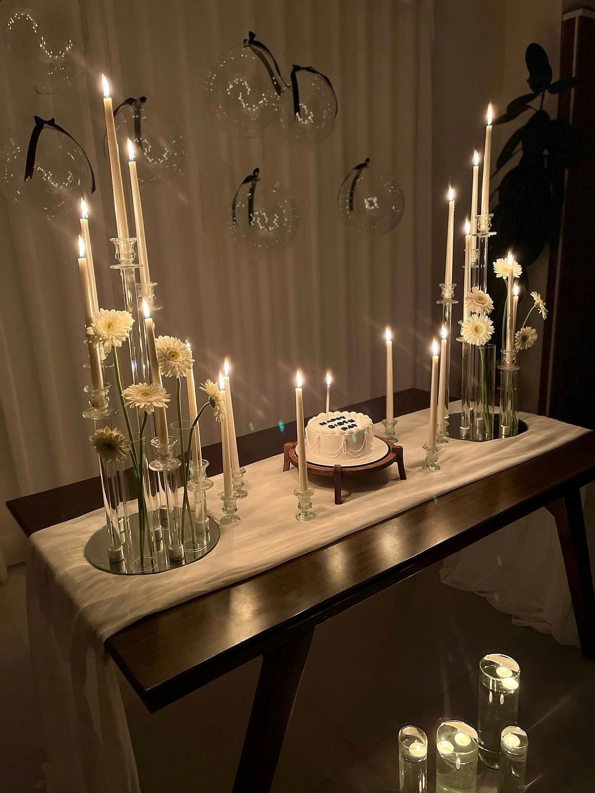 Table setting with tall glass vases, white flowers, and lit taper candles.
