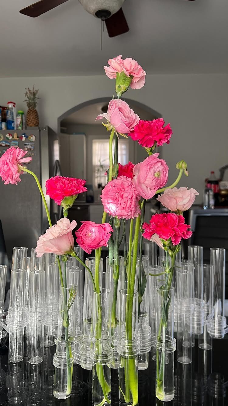 Pink and magenta carnations arranged in clear test-tube vases on a dark table