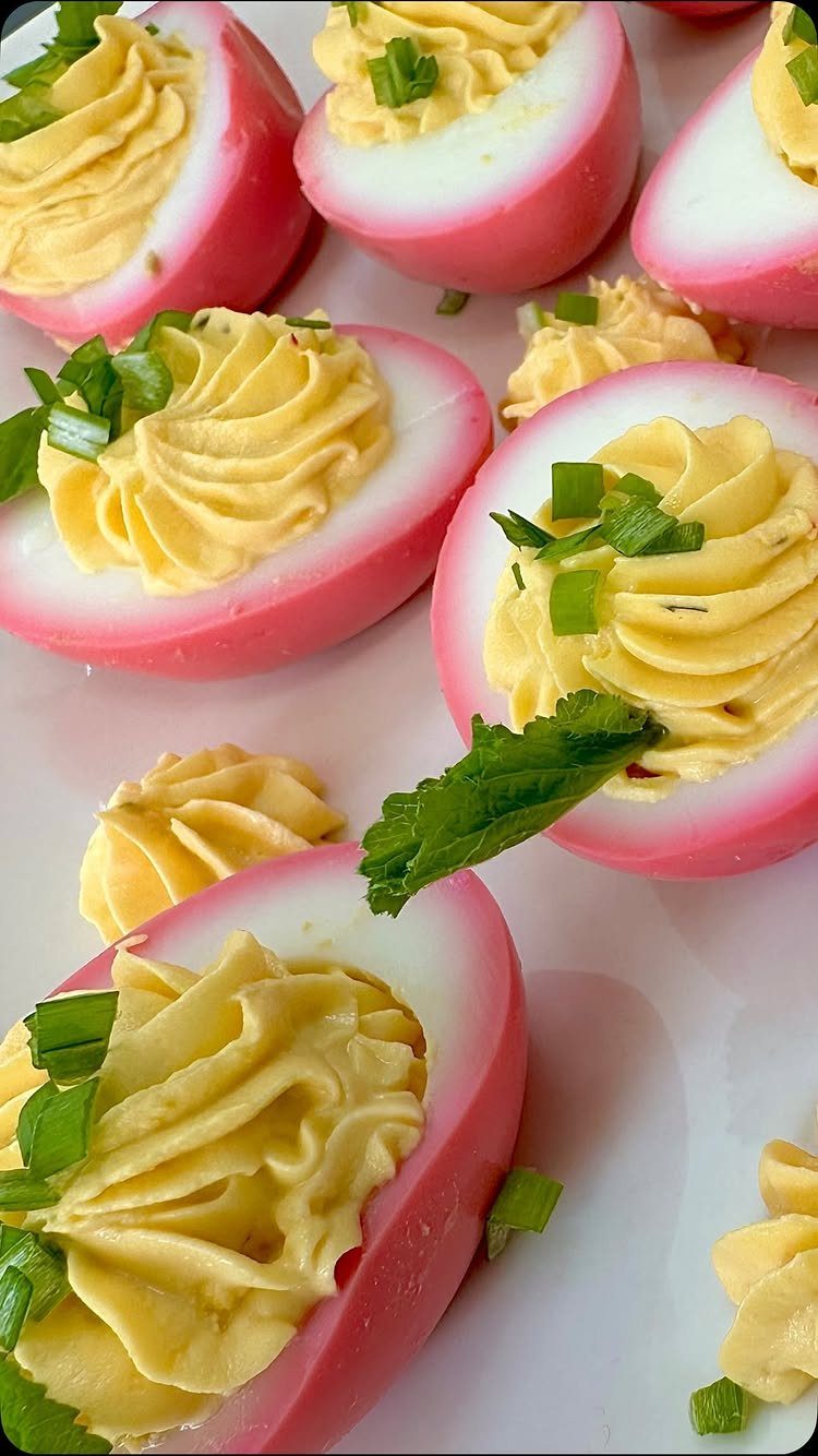 Pink deviled eggs with piped yellow filling and chopped green chives garnish.