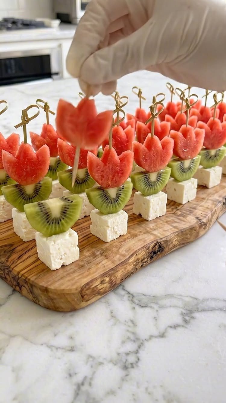 Fruit skewers with watermelon tulips, kiwi, and feta cheese on a wooden board.