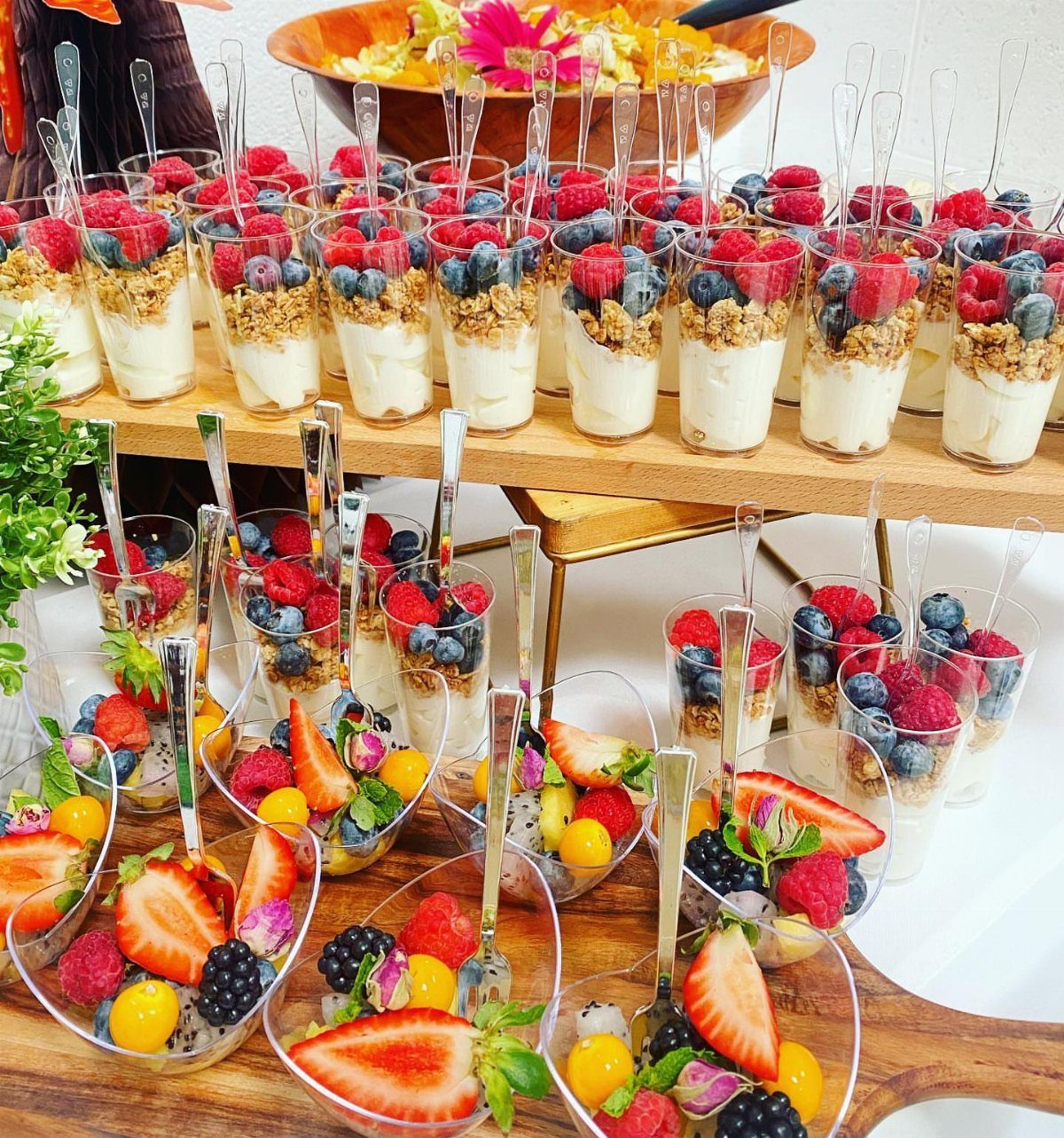 Layered yogurt and fruit parfaits with granola in small glasses on wooden boards.