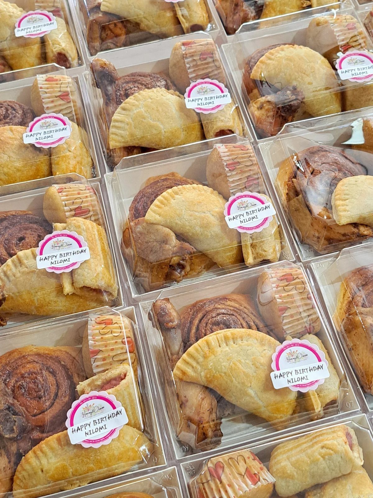 Assorted pastries in clear plastic containers with pink birthday stickers for a party.