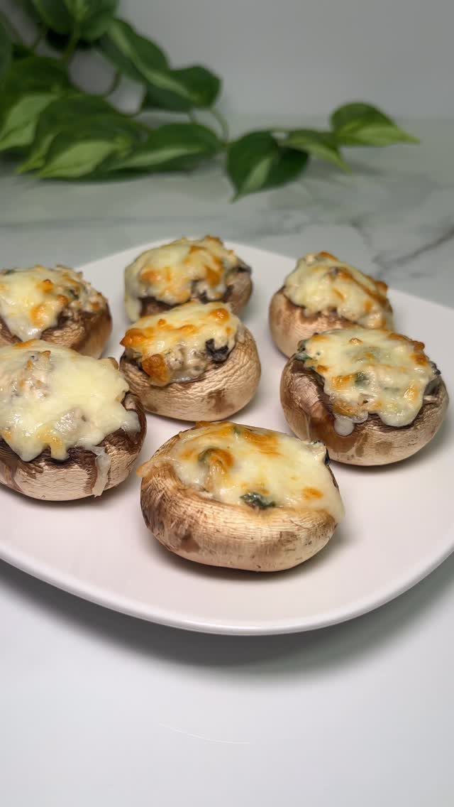 Stuffed mushrooms with melted cheese served on a white plate with green leaves.
