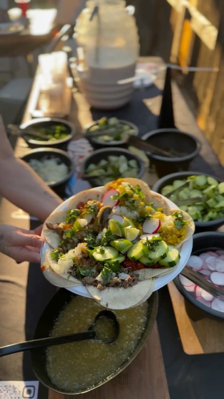 Loaded taco on a plate with a taco station setup in background