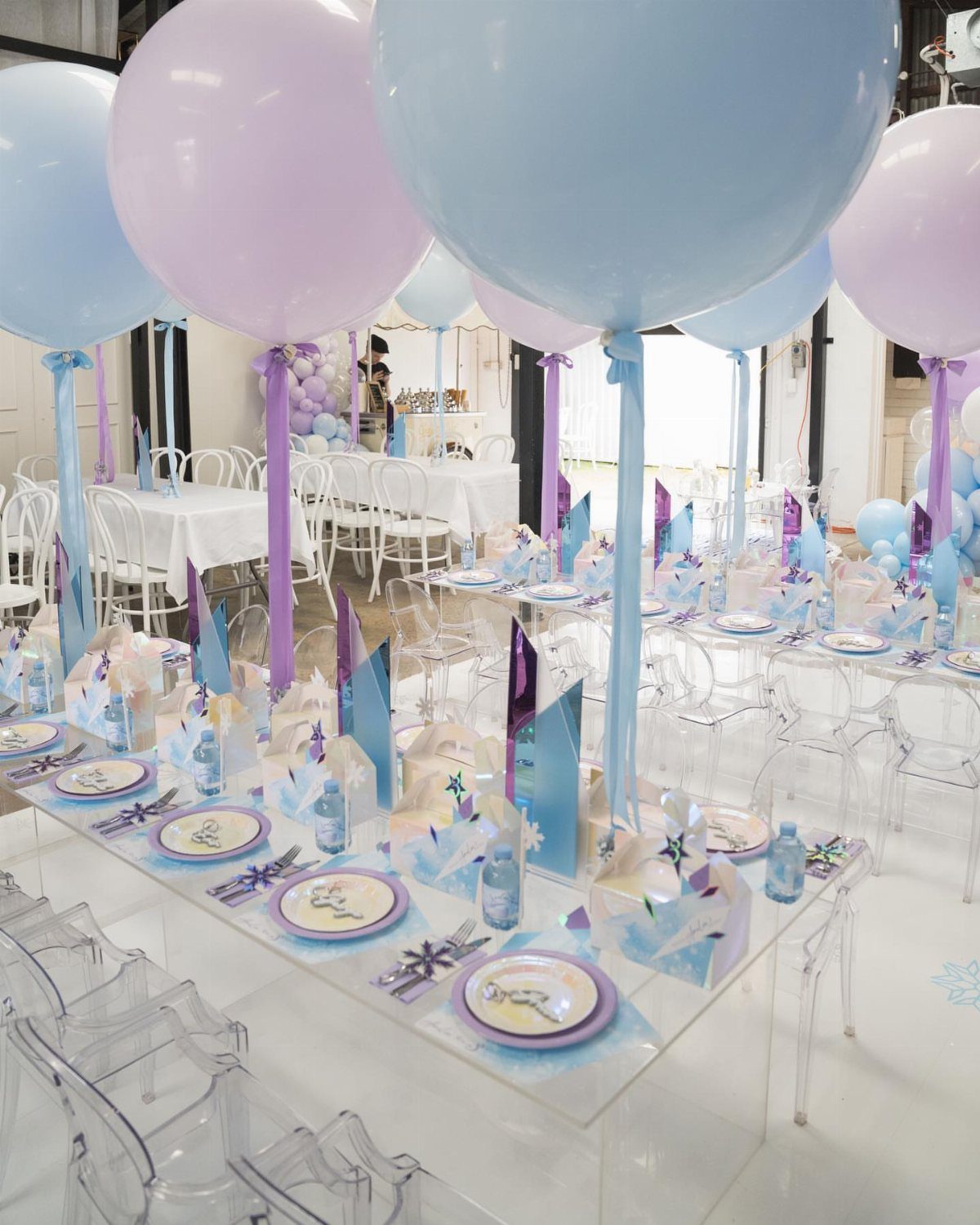 White party table with floating blue and purple balloons and matching place settings.