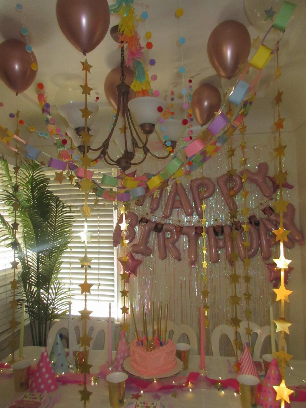 Birthday party table with pink cake, rose gold balloons, and colorful star garlands.