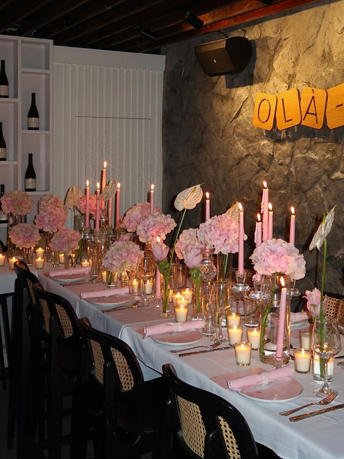 Long dining table decorated with pink hydrangeas and many lit pink taper candles.