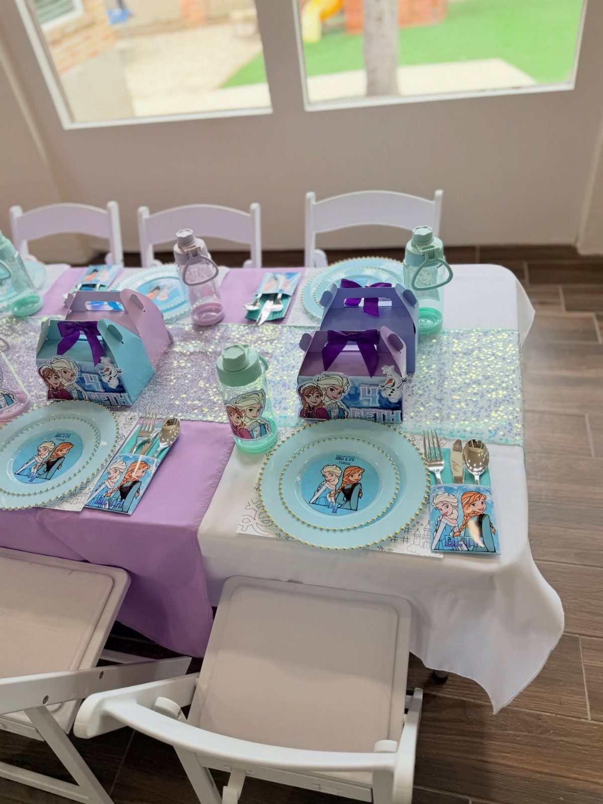 Frozen themed birthday table with blue plates, purple runner, and themed gift boxes.