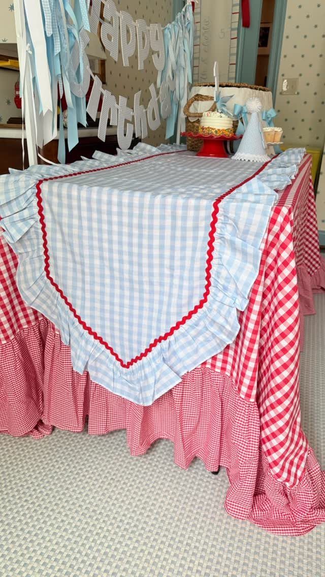 Layered red and blue gingham tablecloths on a birthday table with a cake.
