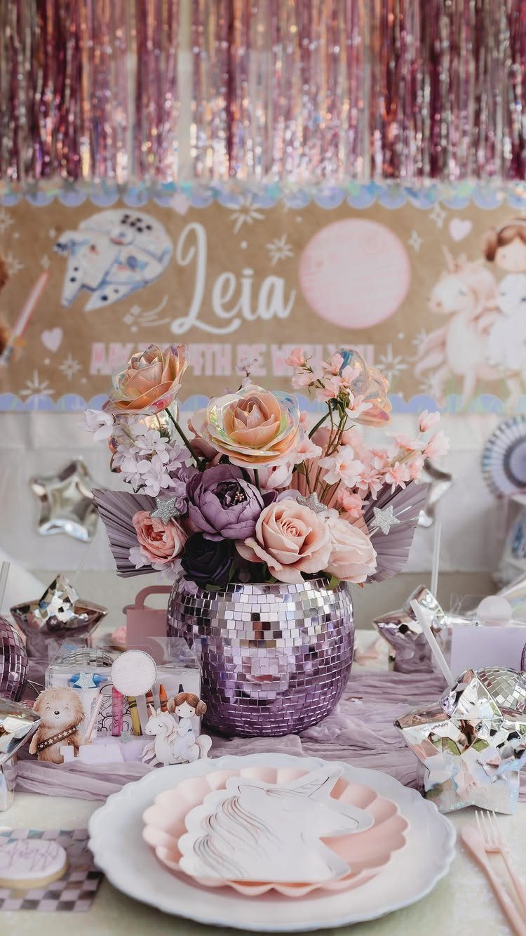 Birthday table with disco ball flower vase, unicorn plates, and pink tinsel backdrop.