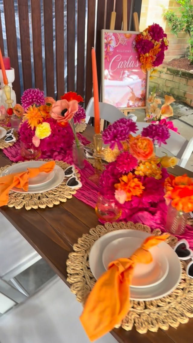 Vibrant pink and orange floral centerpieces on a wooden table with orange napkins.