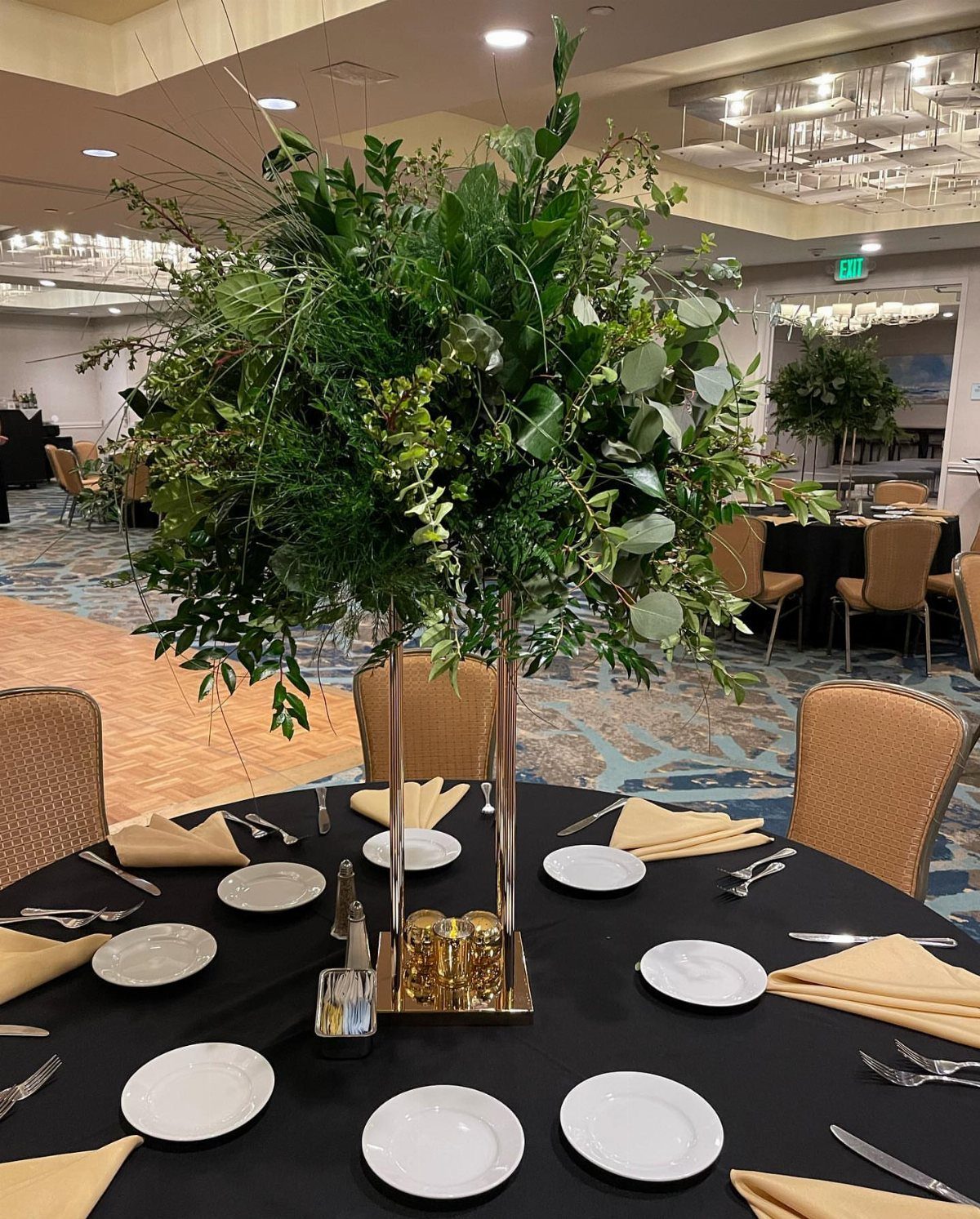 Lush green foliage centerpiece on a gold stand atop a black banquet table.