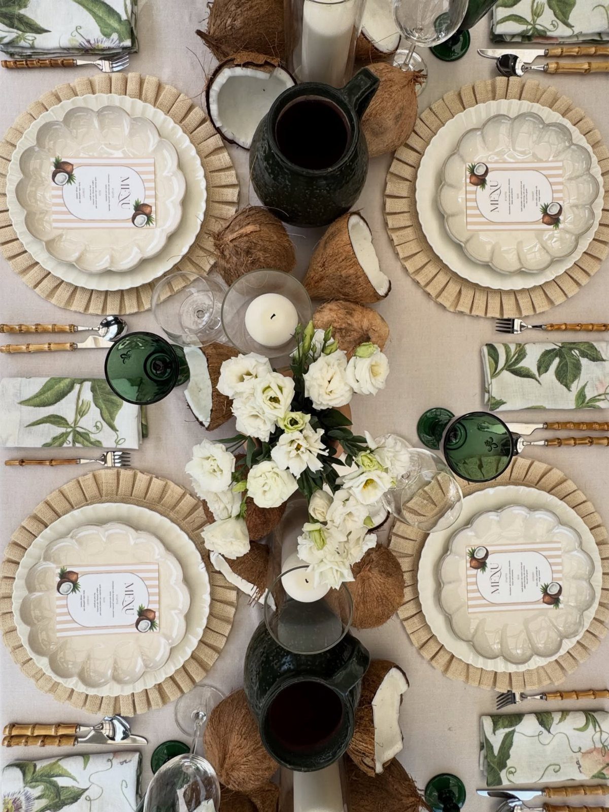 Tropical table setting with white scalloped plates, coconut shells, and white floral centerpieces.