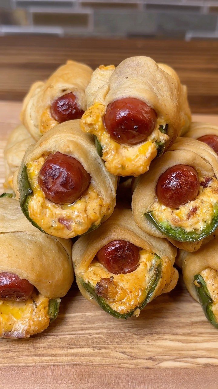 Small sausages wrapped in pastry with melted cheese and peppers on wood.