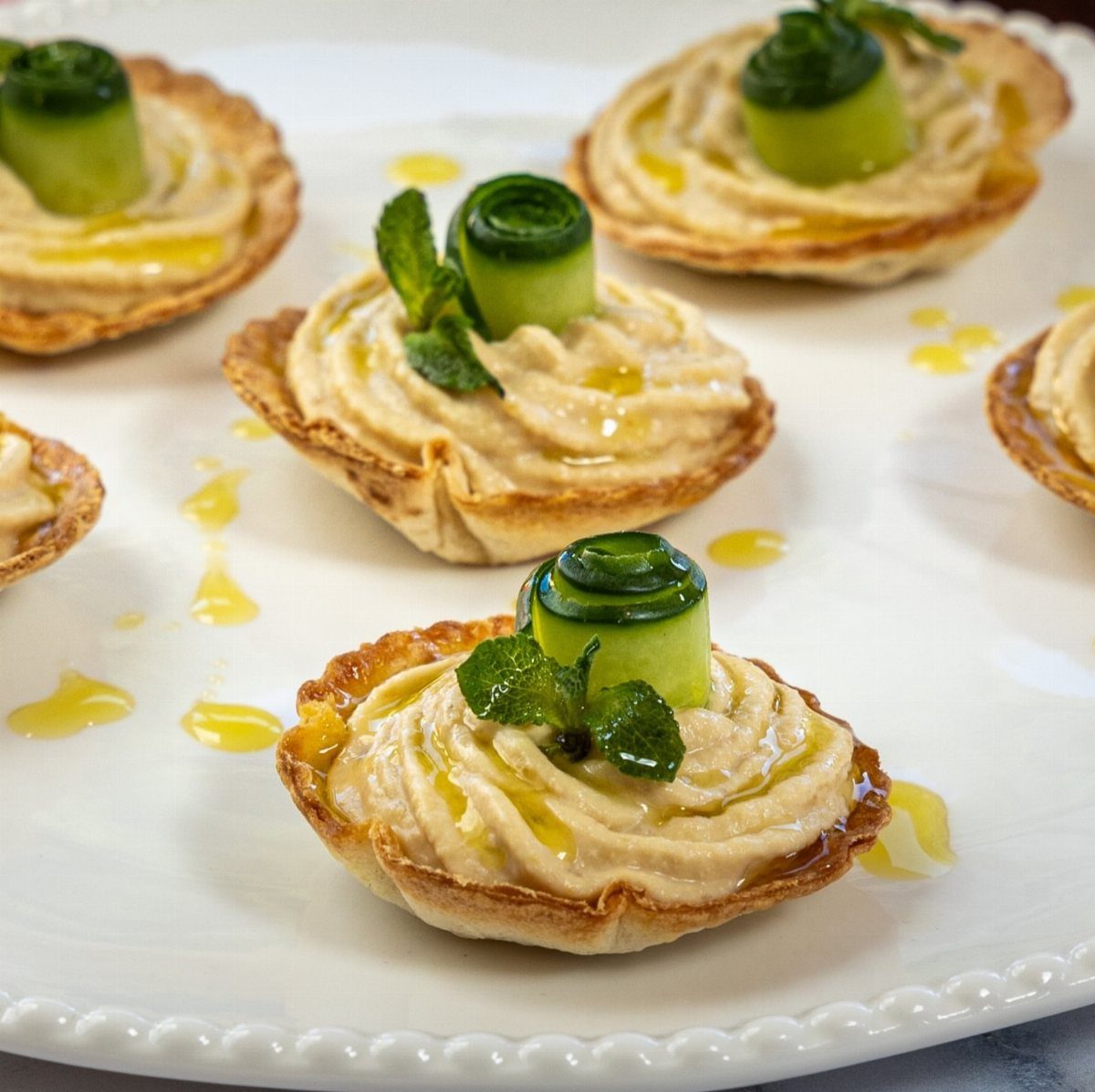 Hummus filled pastry tartlets topped with rolled cucumber and mint on white plate