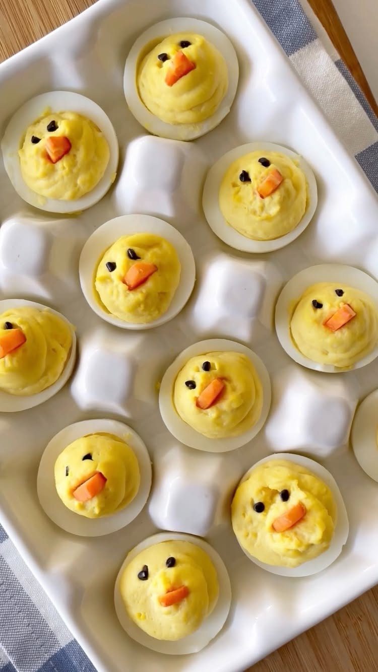 Deviled eggs decorated as yellow chicks in a white ceramic egg tray.