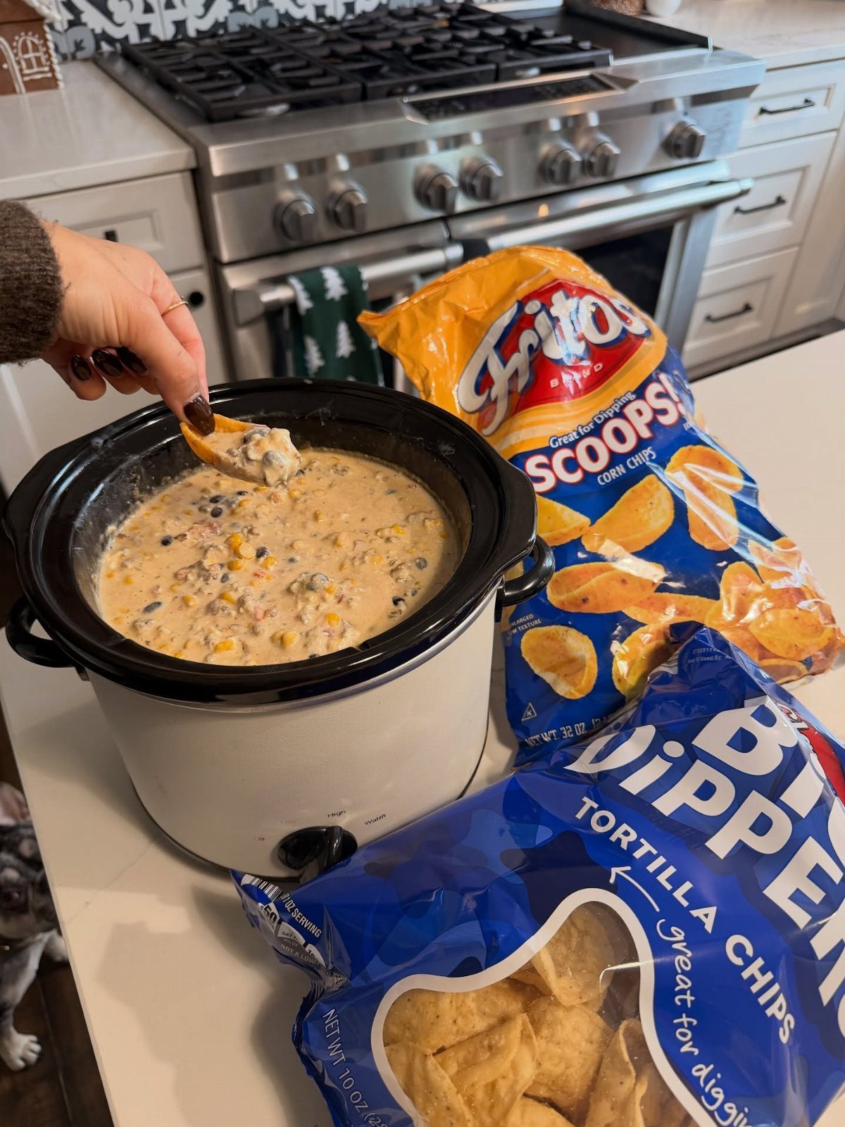 Creamy corn dip in a slow cooker with bags of corn chips nearby.