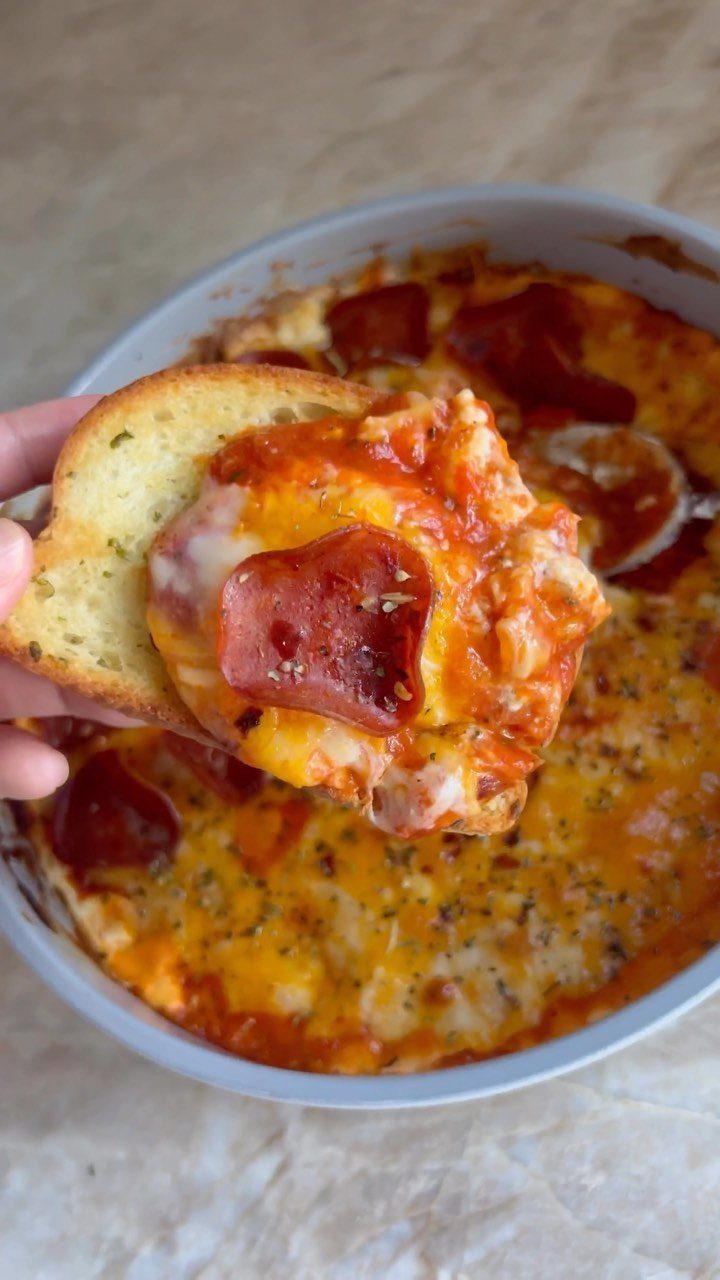 Toasted garlic bread scooping cheesy pizza dip with pepperoni from a white dish.