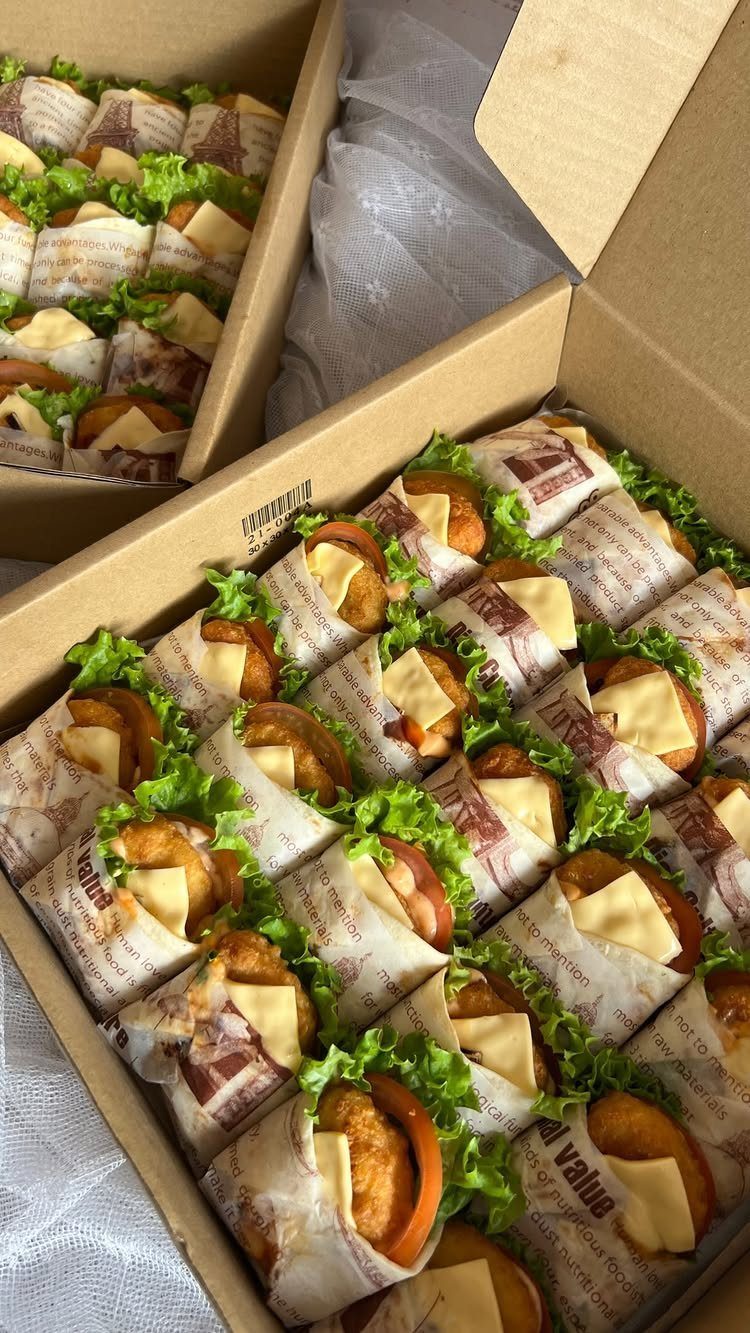 Small wrap appetizers with fried patties, cheese, and lettuce in cardboard boxes.