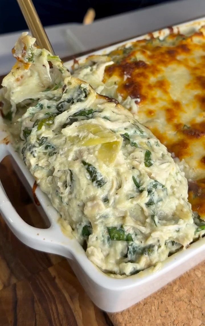 Creamy spinach artichoke dip being scooped from a white ceramic baking dish.
