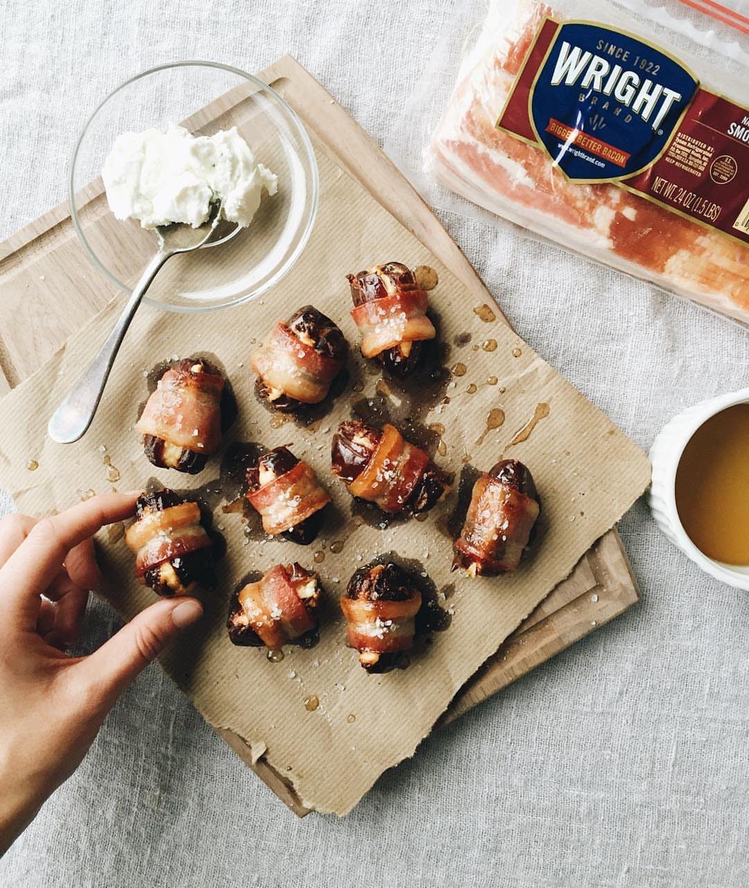 Bacon-wrapped dates with cheese crumbles on parchment paper next to a dip bowl.