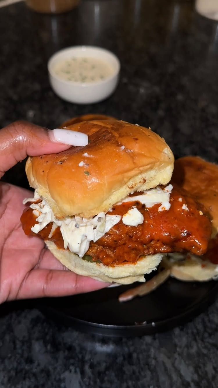 Buffalo chicken slider with creamy topping held in a hand over a black plate.