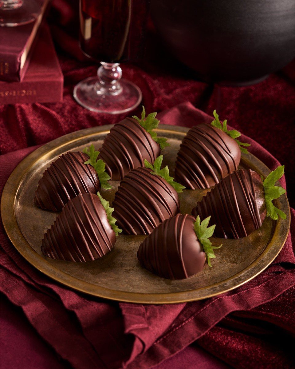 Chocolate-covered strawberries with drizzle on a gold plate over red fabric.