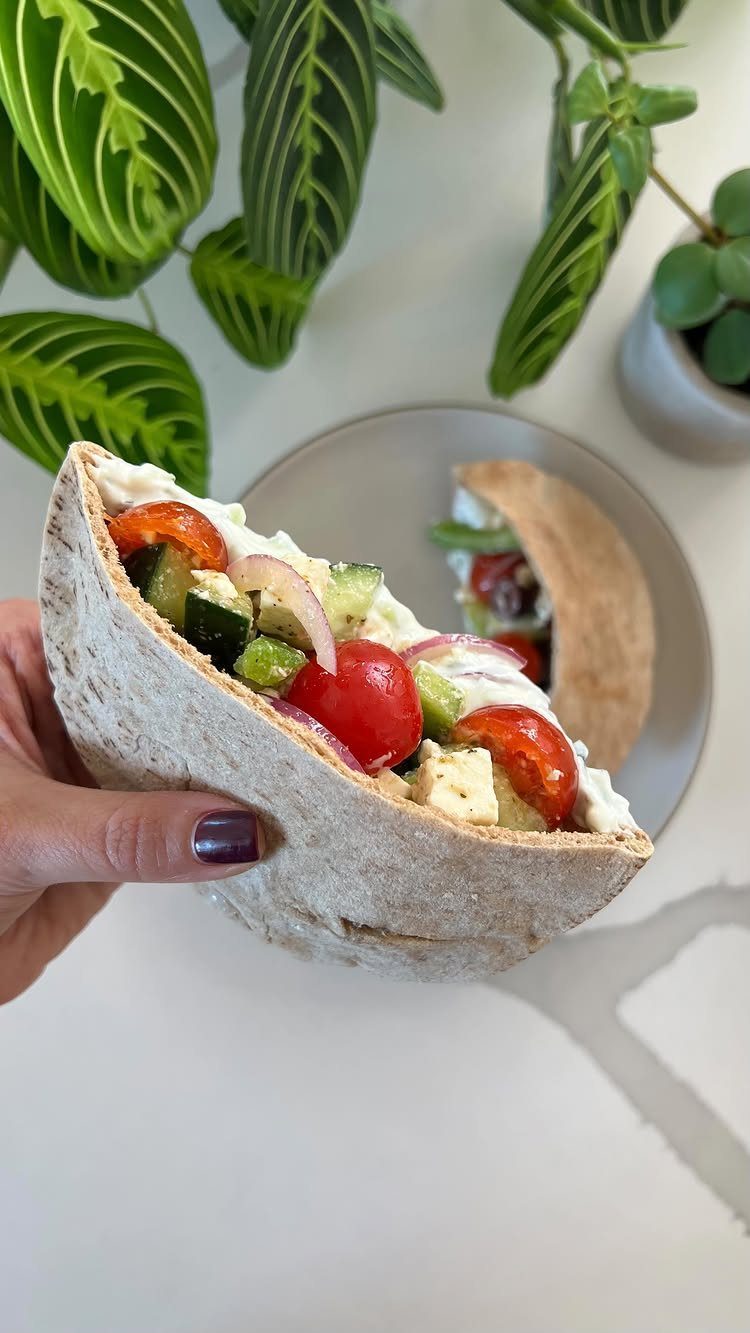 Pita bread cups filled with Greek salad ingredients held over a grey plate.