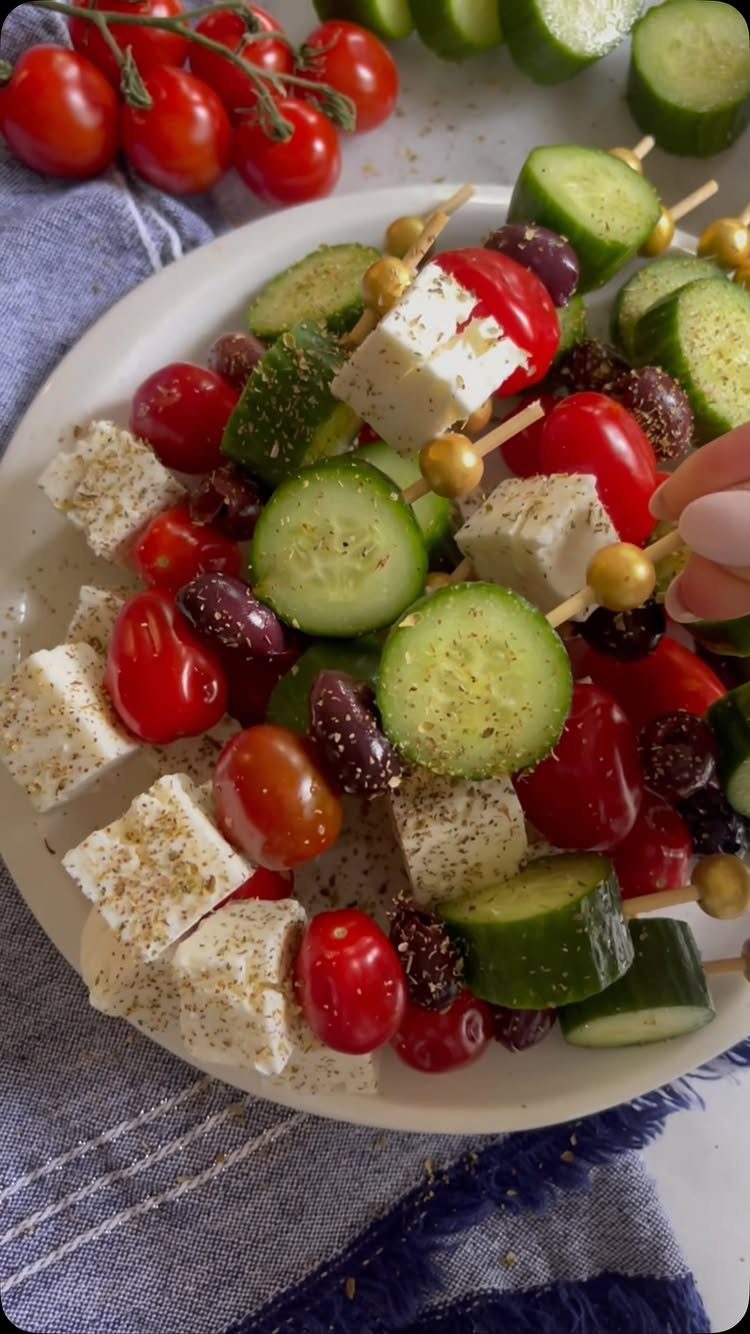 Greek salad skewers with feta, cucumber, and tomatoes on a white plate.