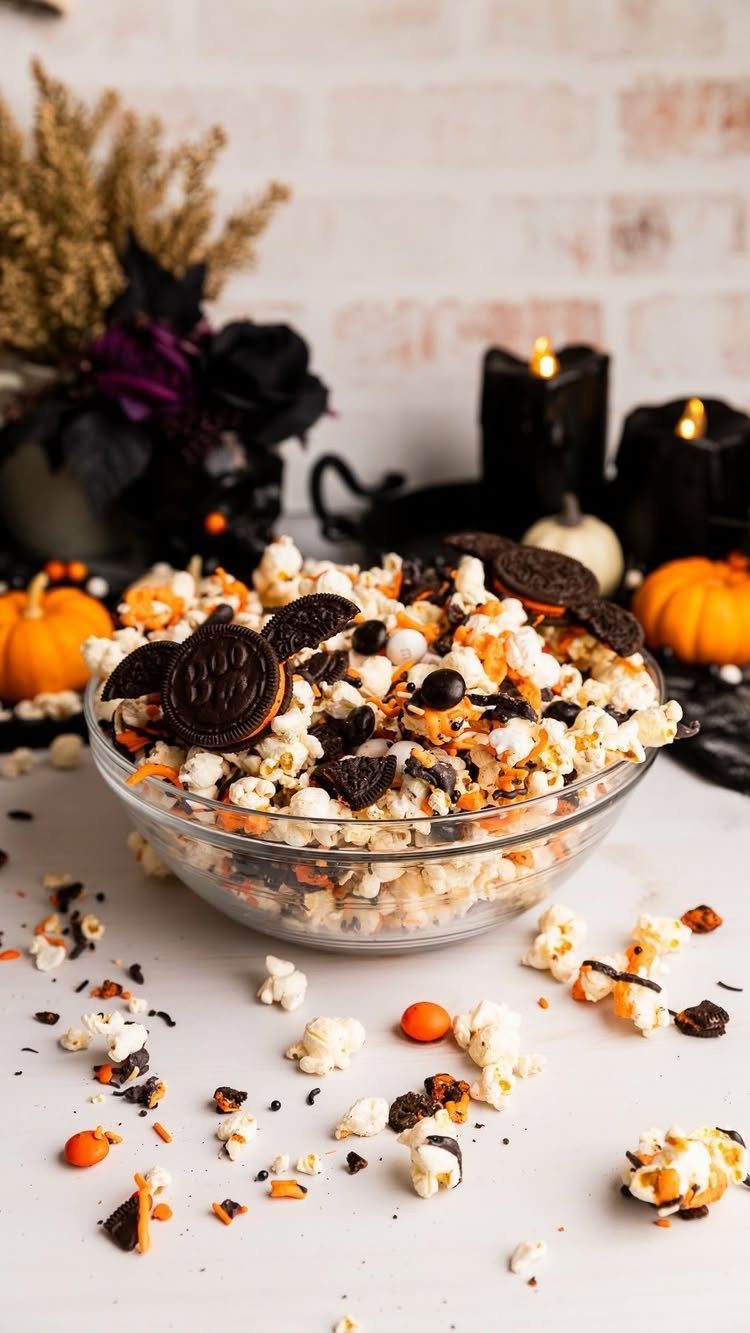 Popcorn mixed with chocolate sandwich cookies and orange candies in a glass bowl.
