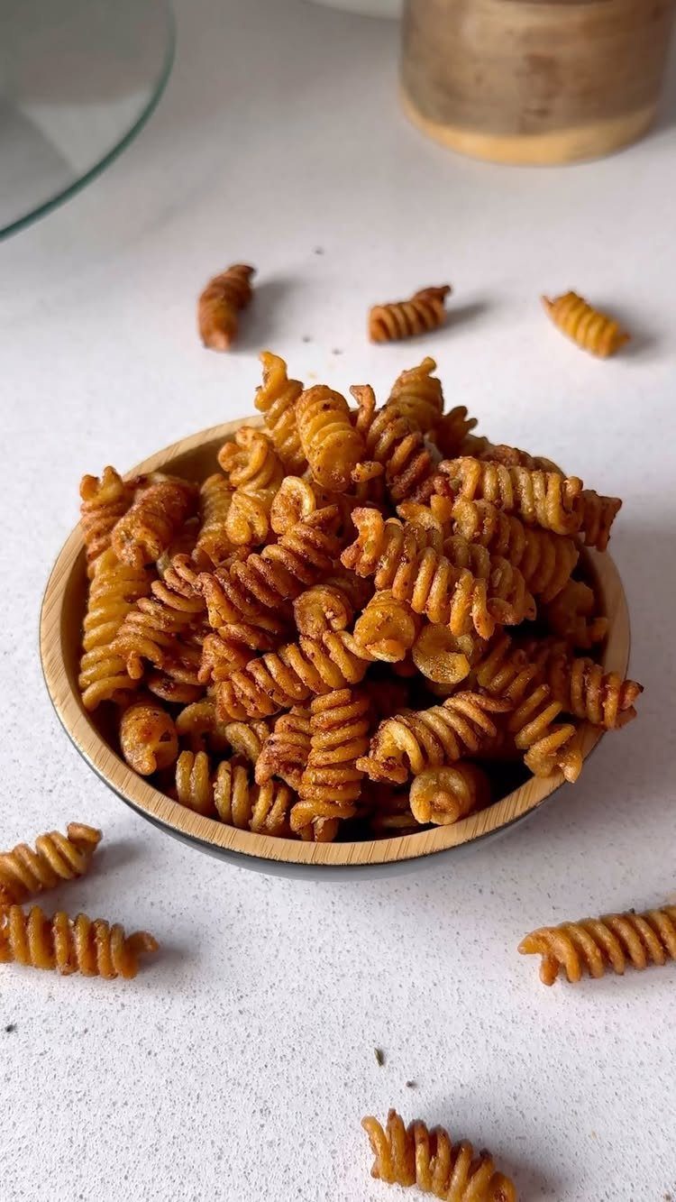 Golden-brown seasoned rotini pasta chips in a small wooden bowl on white surface.