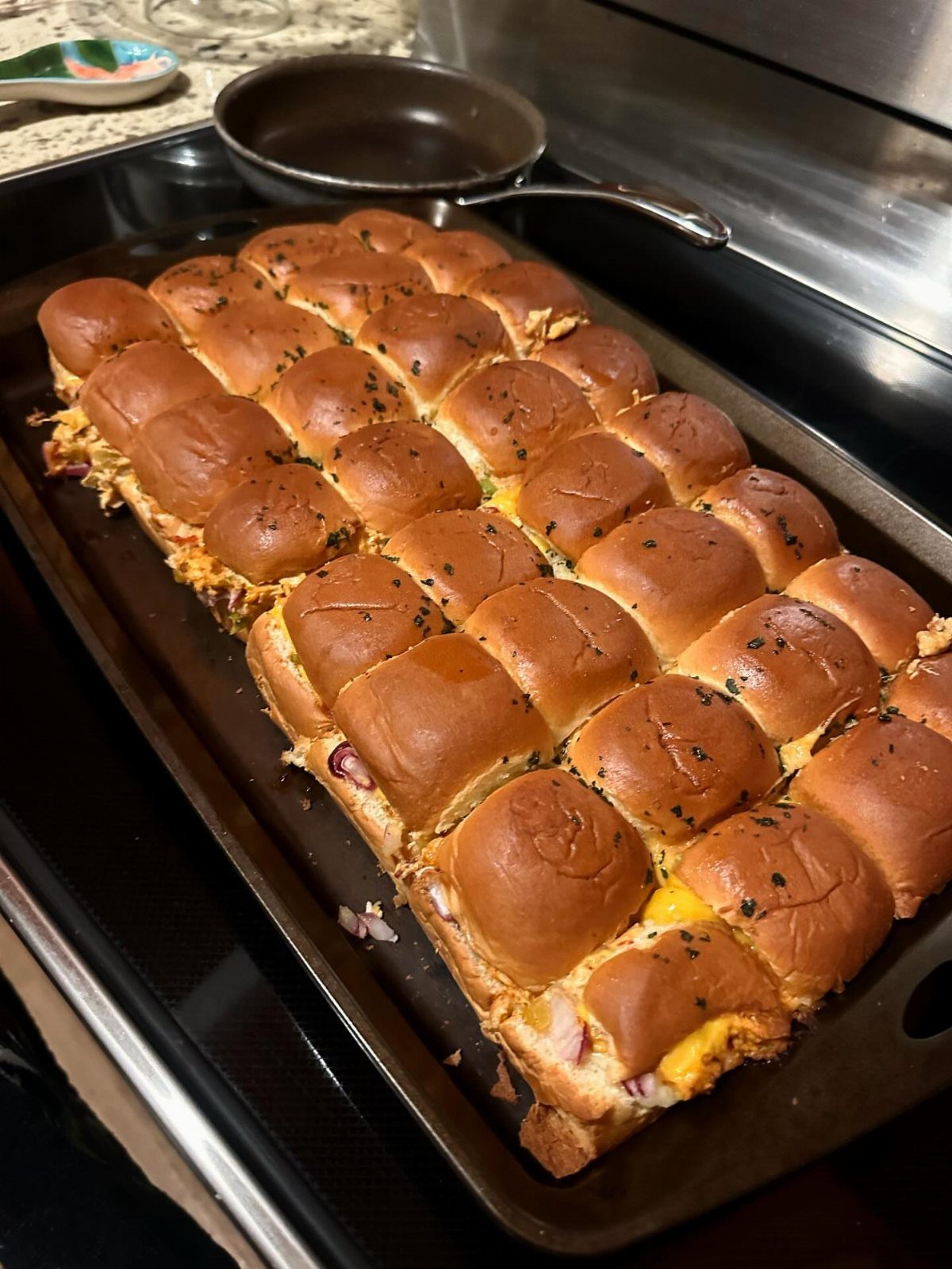 Golden-brown pulled chicken sliders with melted cheese on a dark baking sheet.