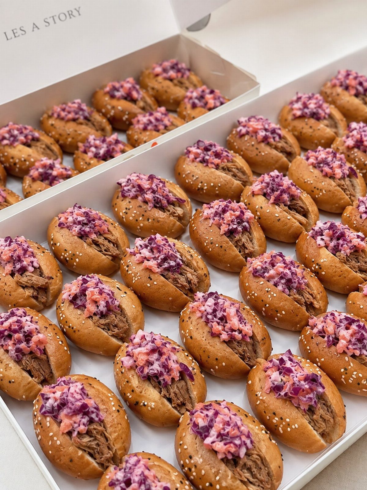 Pulled pork sliders with purple coleslaw arranged in white catering boxes.