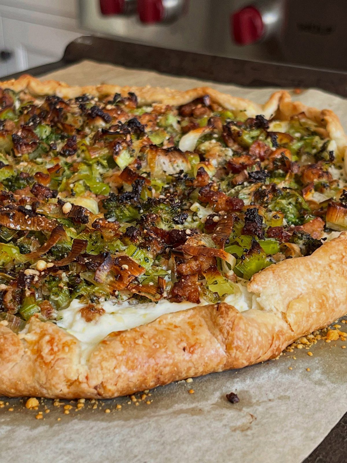 Savory galette with roasted broccoli, leeks, and bacon on a baking sheet.