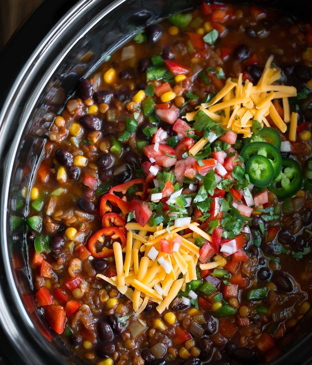 Hearty chili in a slow cooker topped with cheese, tomatoes, and jalapeños.