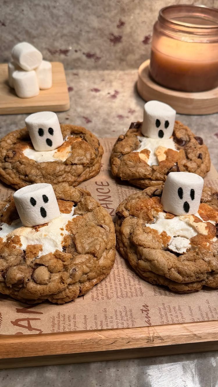 S'mores cookies topped with melted marshmallows and tiny marshmallow ghosts on a board.