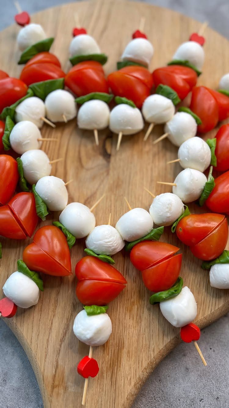 Heart-shaped Caprese skewers with tomatoes and mozzarella on a wooden board.